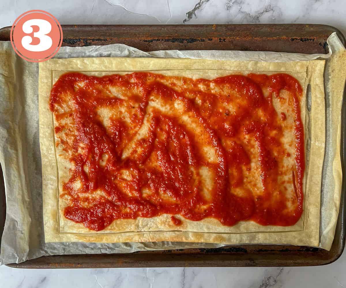 a puff pastry sheet covered in tomato sauce.
