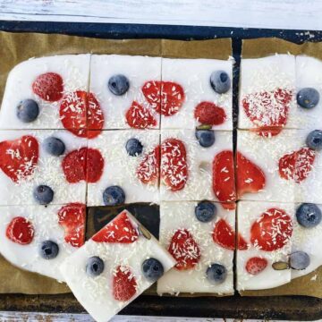 Yoghurt bark with blueberries and strawberries on a baking tray cut into pieces.