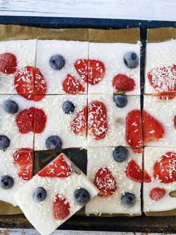 Yoghurt bark with blueberries and strawberries on a baking tray cut into pieces.