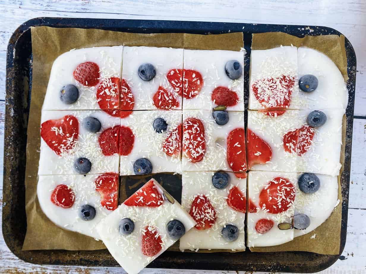 Yoghurt bark with blueberries and strawberries on a baking tray cut into pieces.