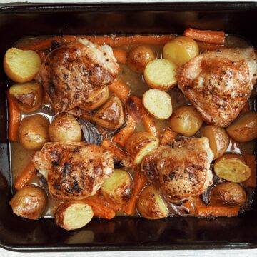 roasted chicken thighs with potatoes and carrots in roasting tin