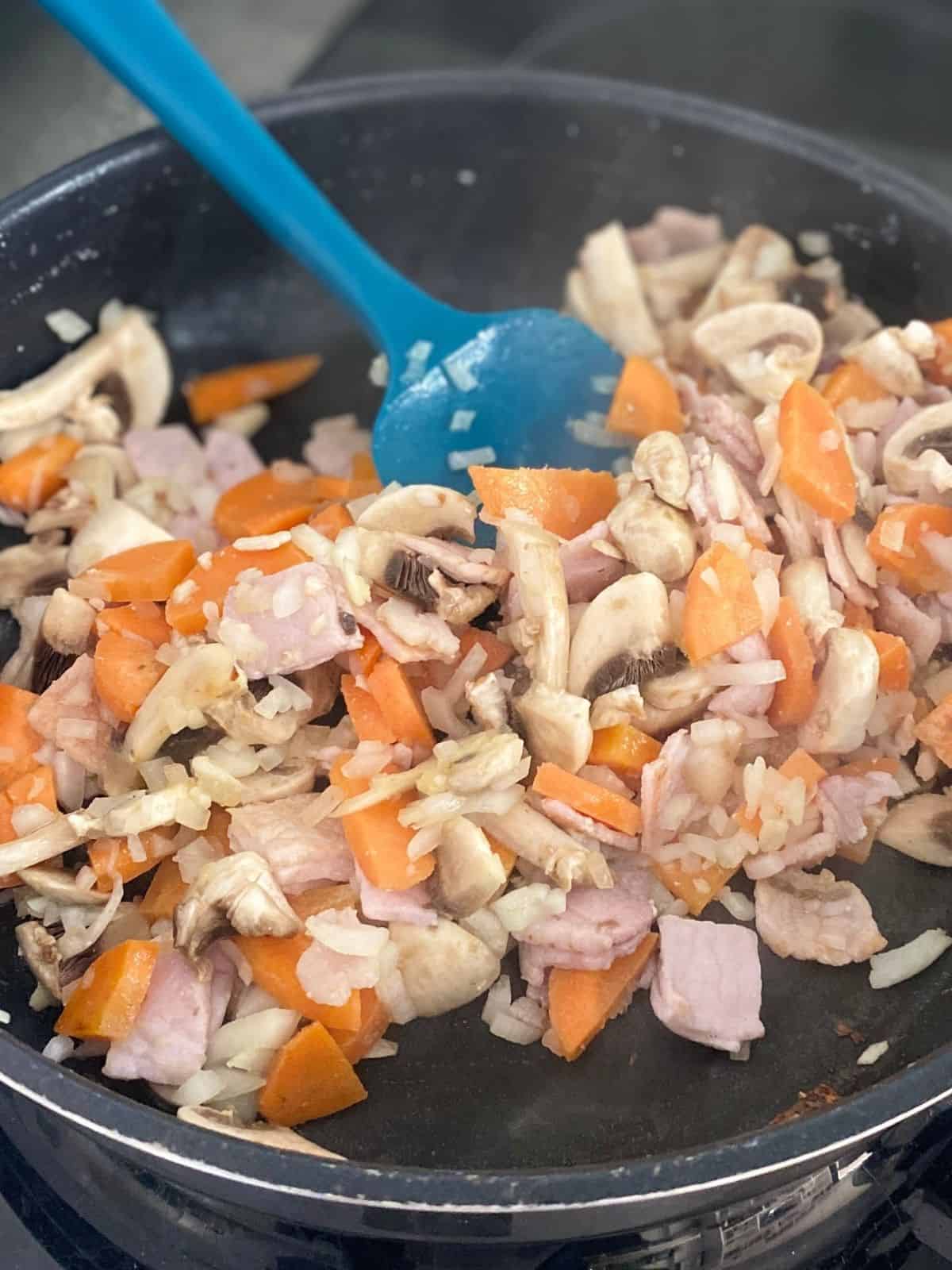 bacon mushrooms and carrots frying in a pan