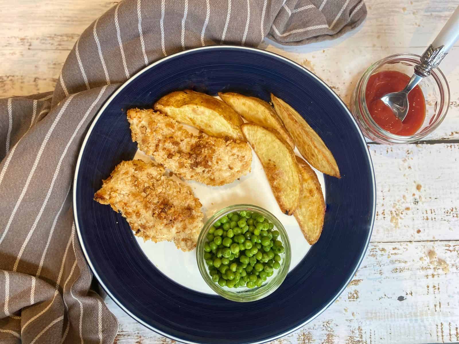 chicken goujons on a plate with potato wedges and peas