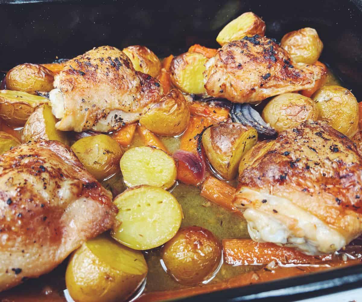 roasted chicken thighs potatoes and carrots in a roasting tin