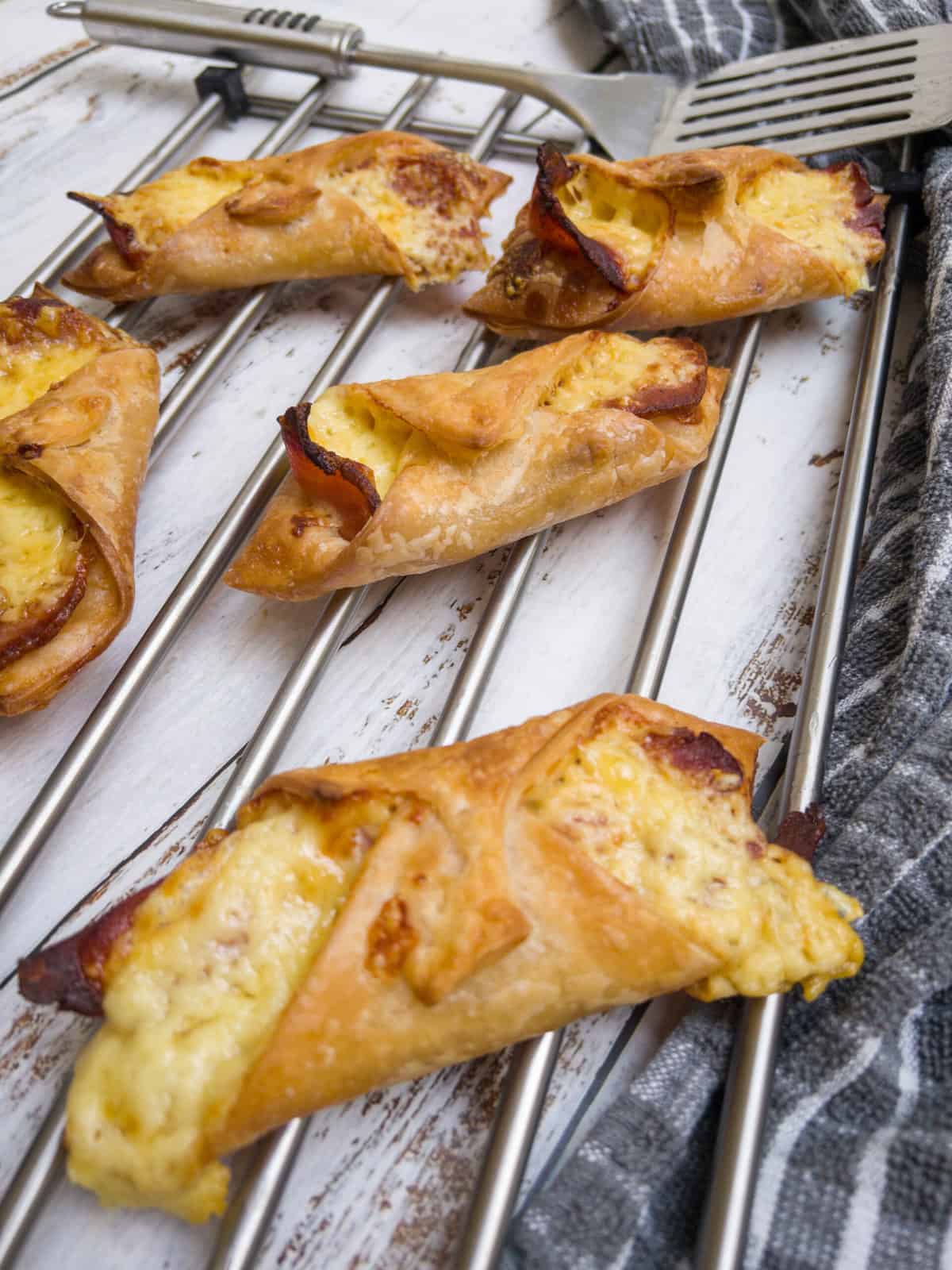 cheese and bacon turnovers on a silver cooling tray with a spatula