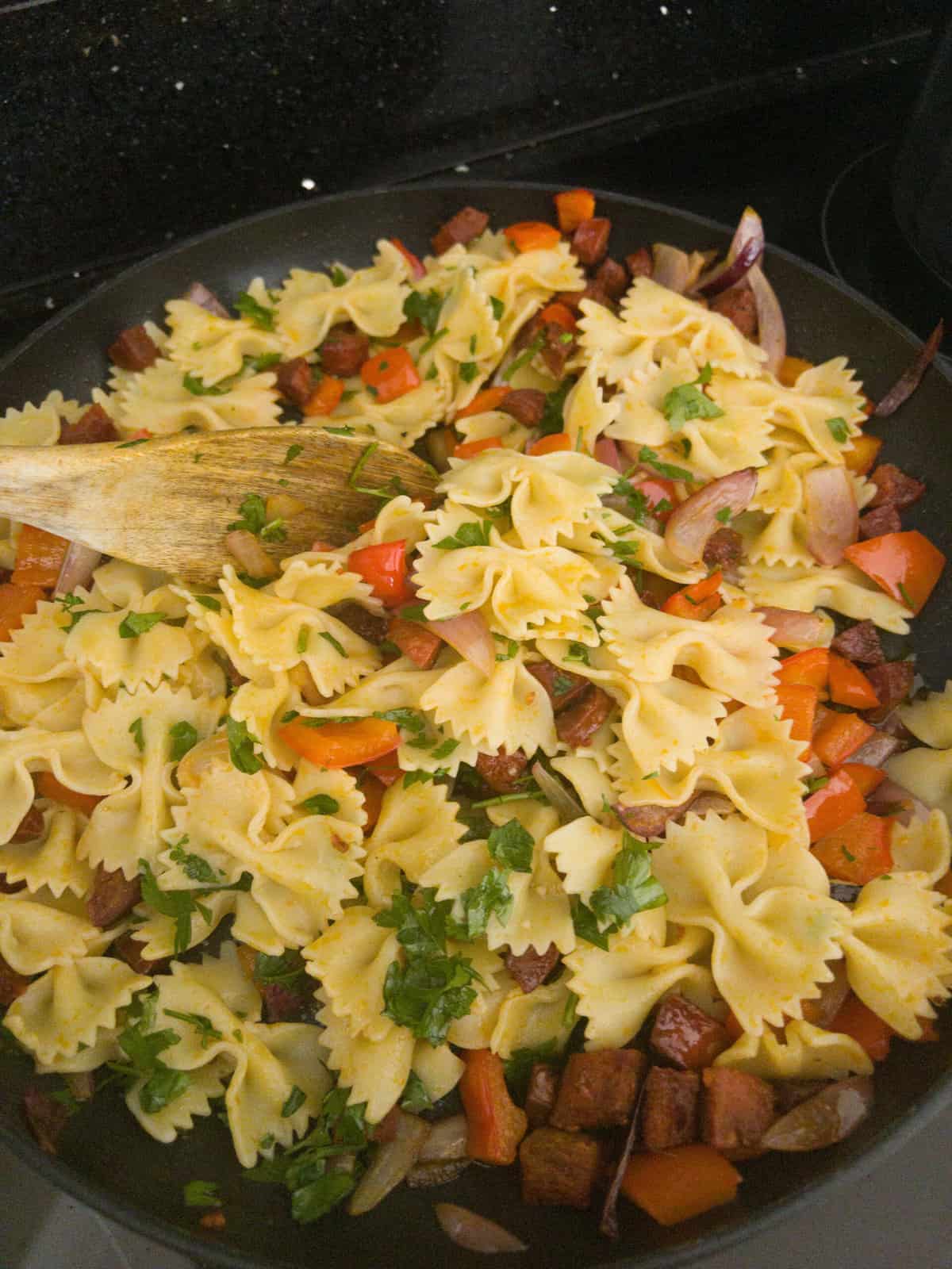pasta with chorizo red peppers and red onion and parsley being mixed in a frying pan