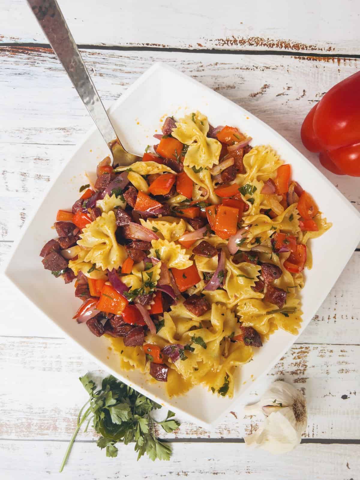 chorizo and red pepper pasta salad with bowtie pasta in a white bowl