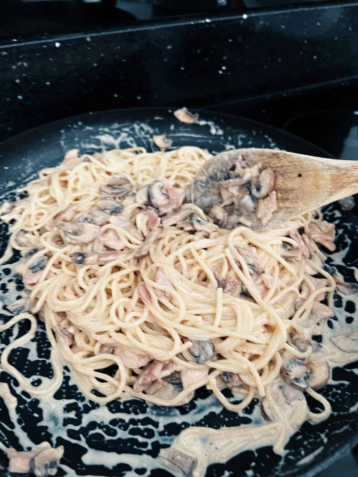 Spaghetti being mixed with carbonara. sauce in a frying pan