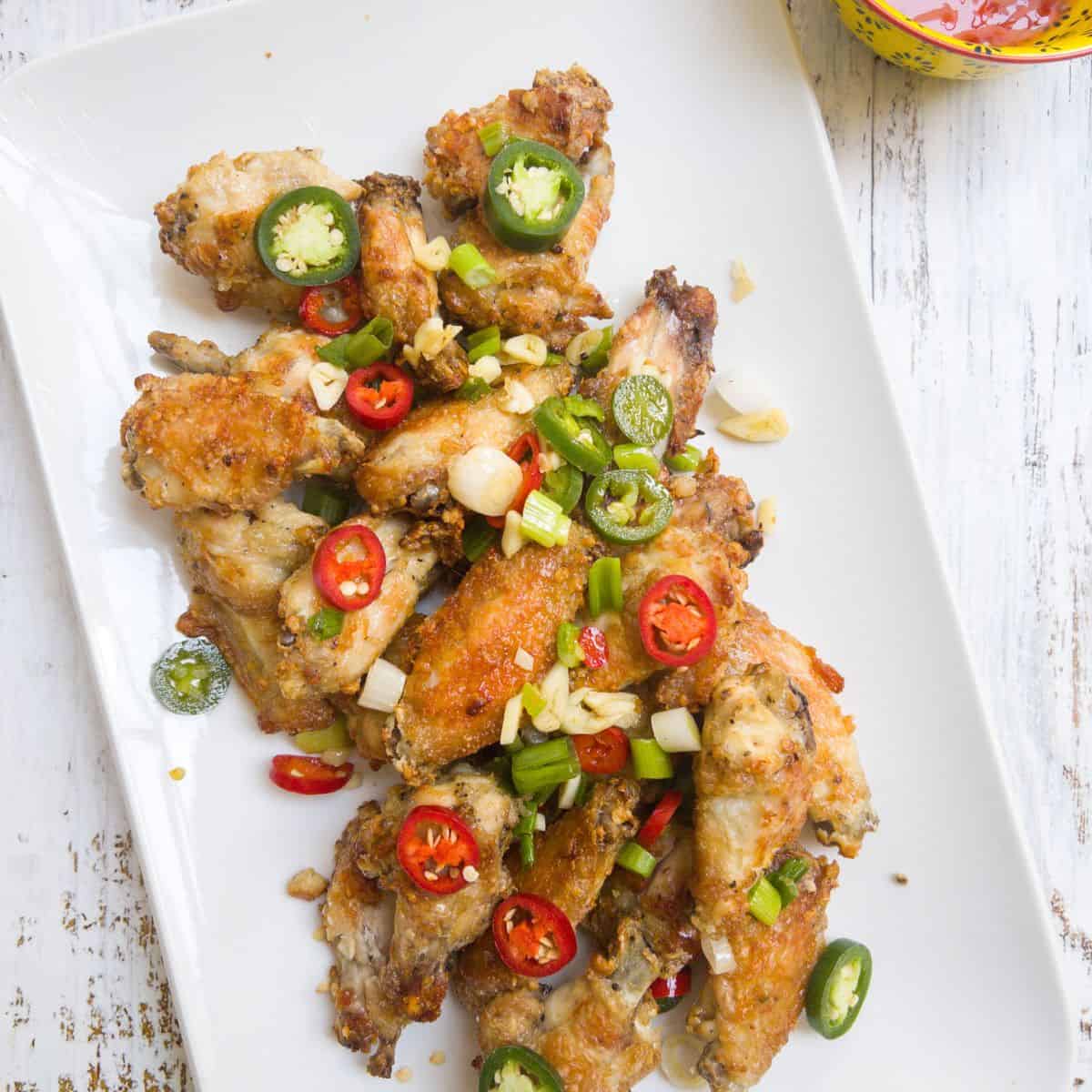 salt and pepper chicken wings garnished with chilli and spring onion on a white serving plate
