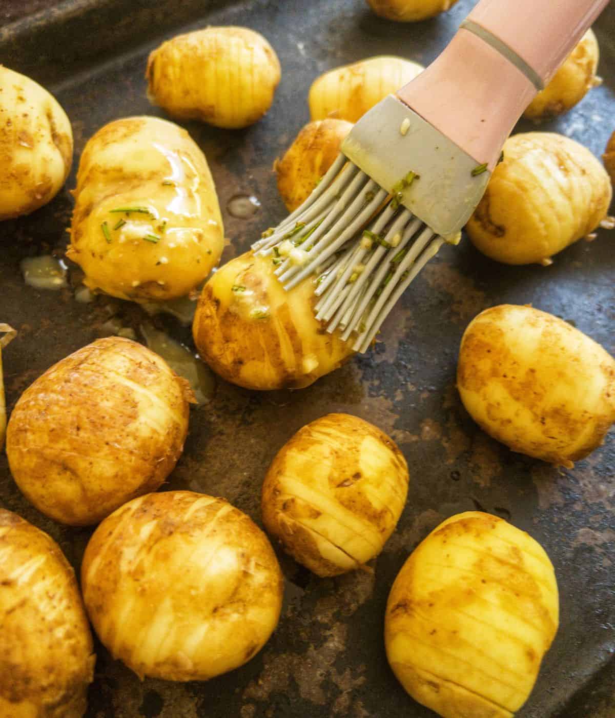 hasselback potatoes being basted with garlic butter and oil