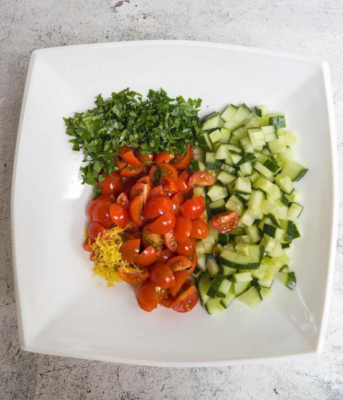 Chopped tomatoes, cucumber, basil parsley and lemon in a white bowl