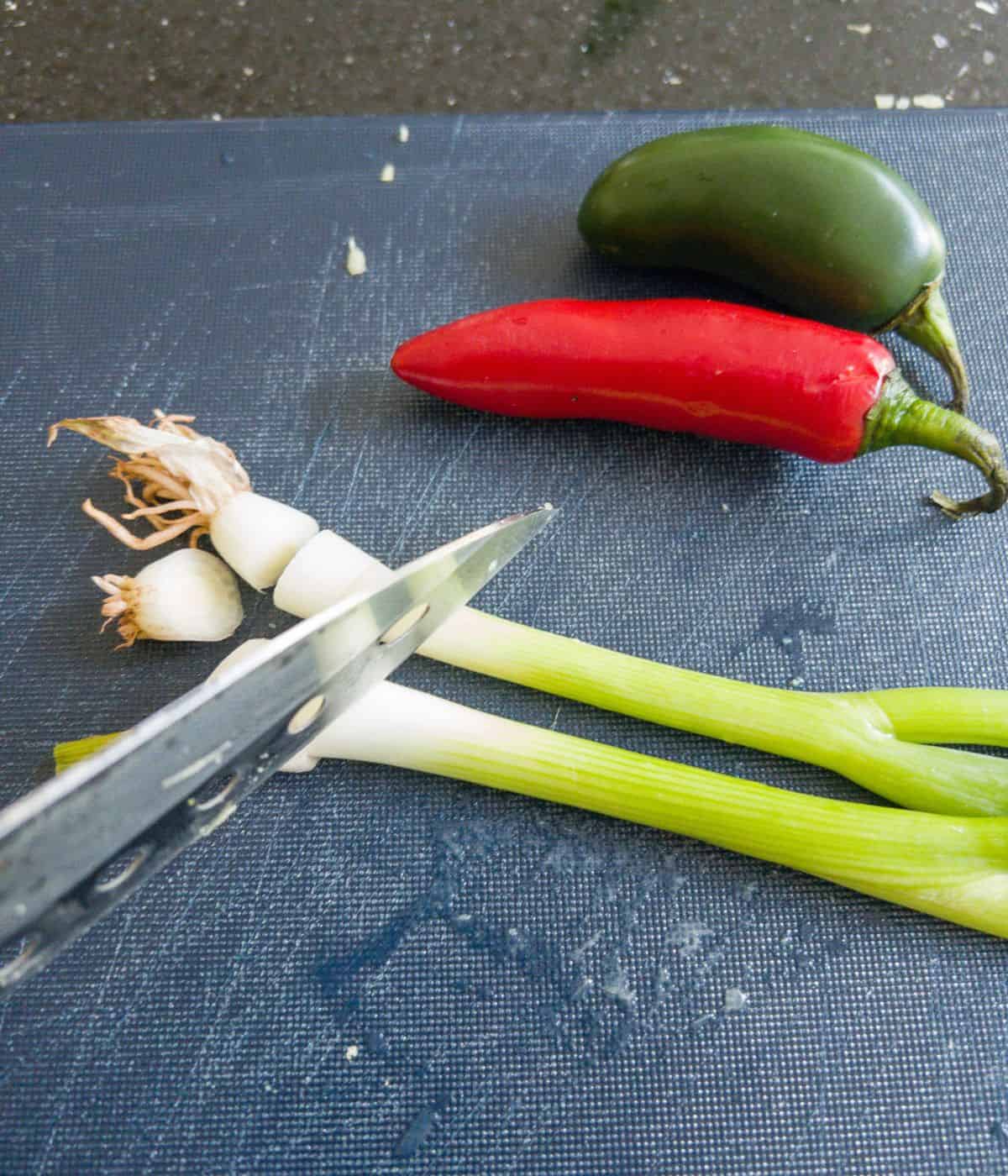 chillis and spring onions being cut with a knife on a blue chopping board