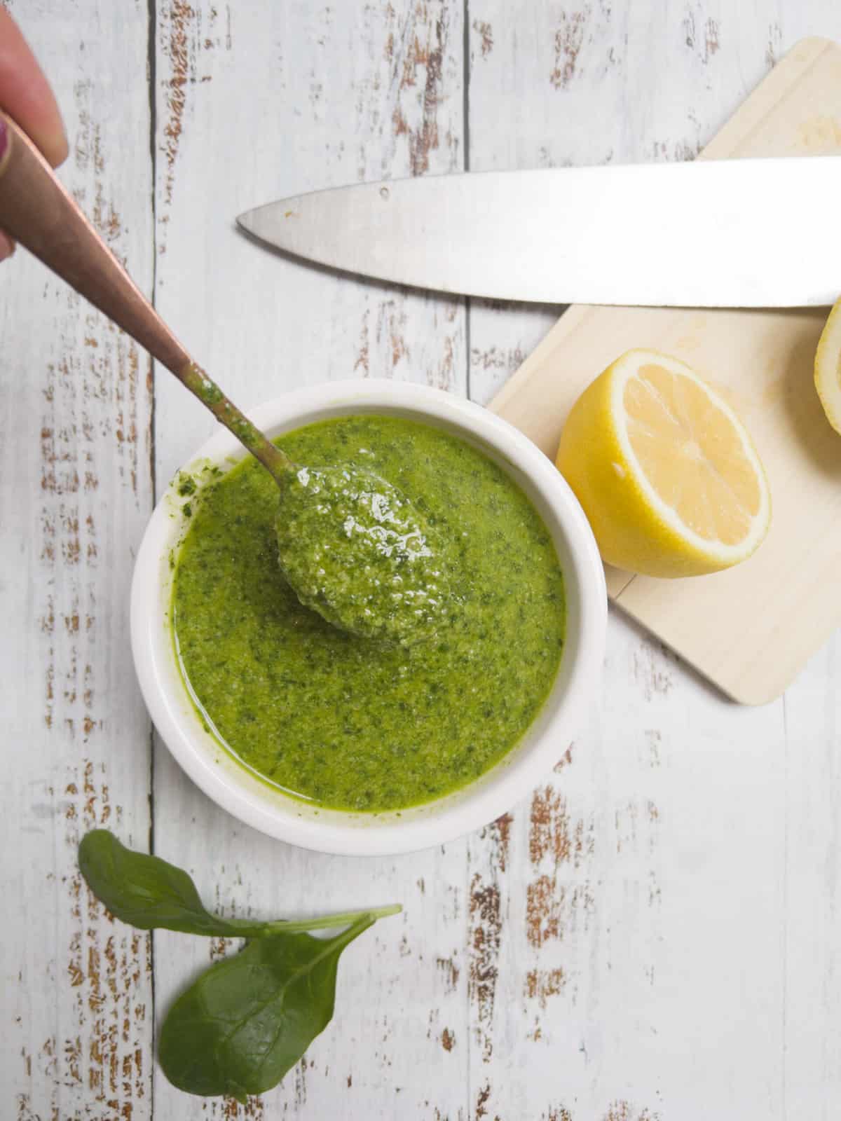 green basil pesto in a white bowl that has a spoon in it.
