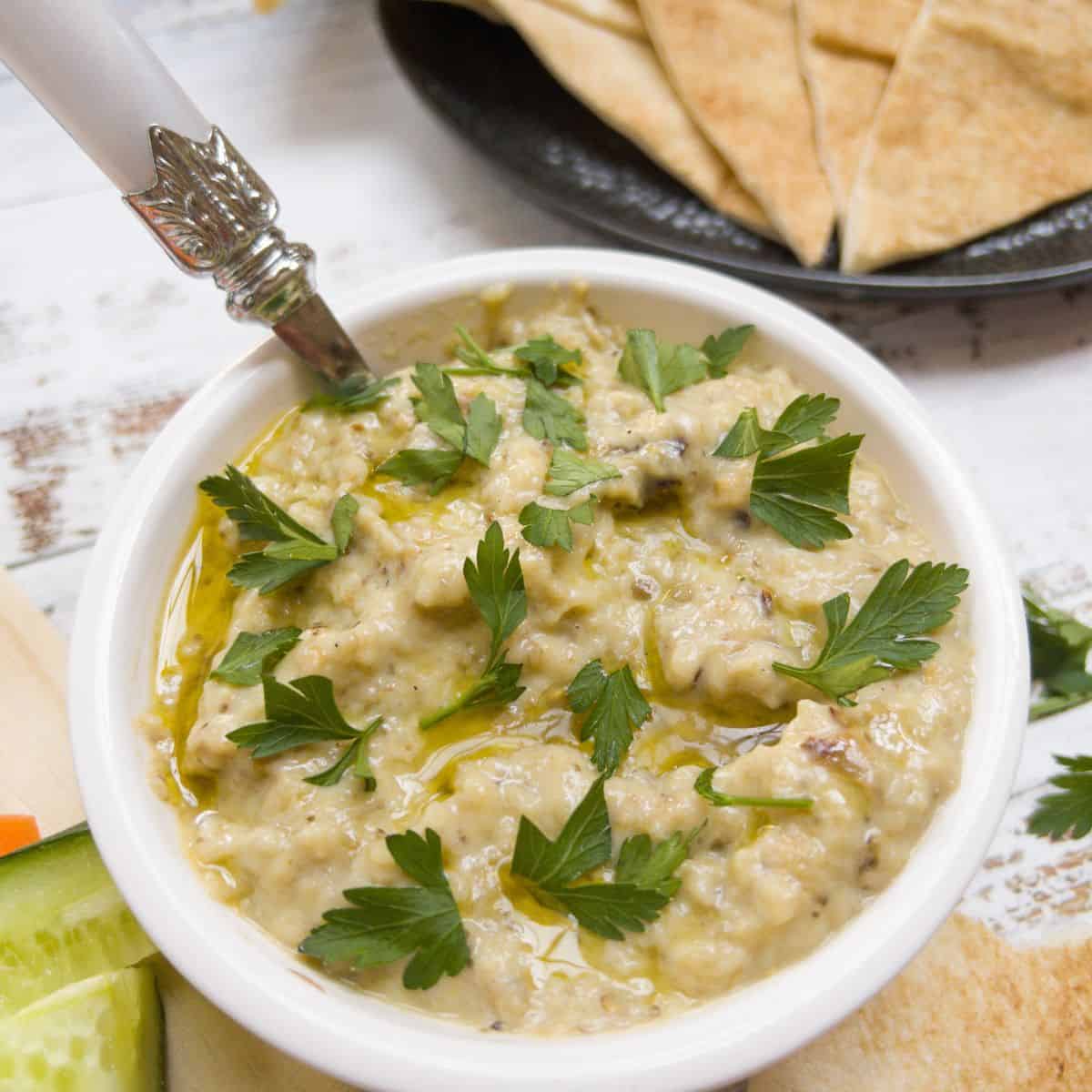 close up picture of baba ganoush in a bowl with some flatbread on the side.