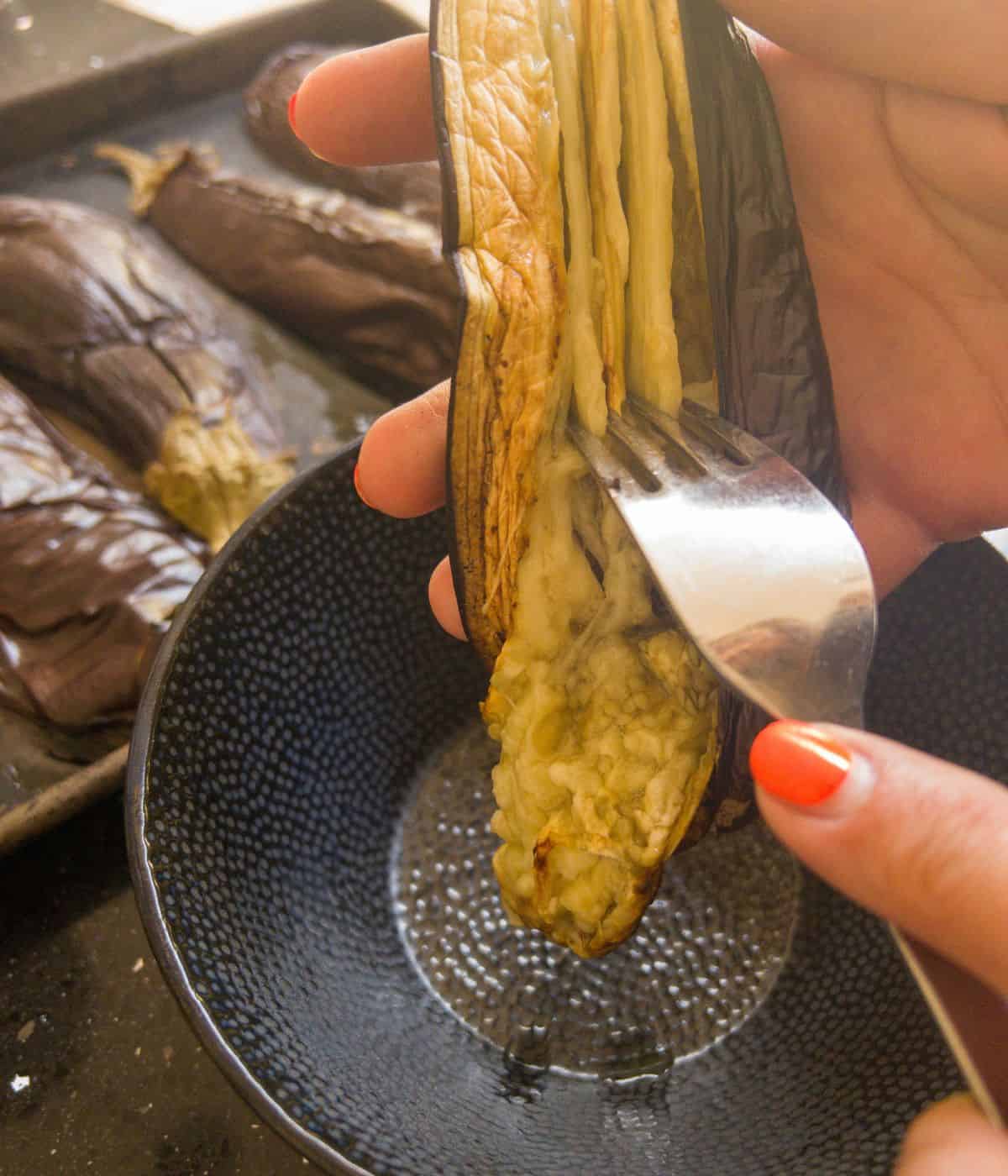 The inside of a roasted aubergine being scraped out with a fork into a bowl