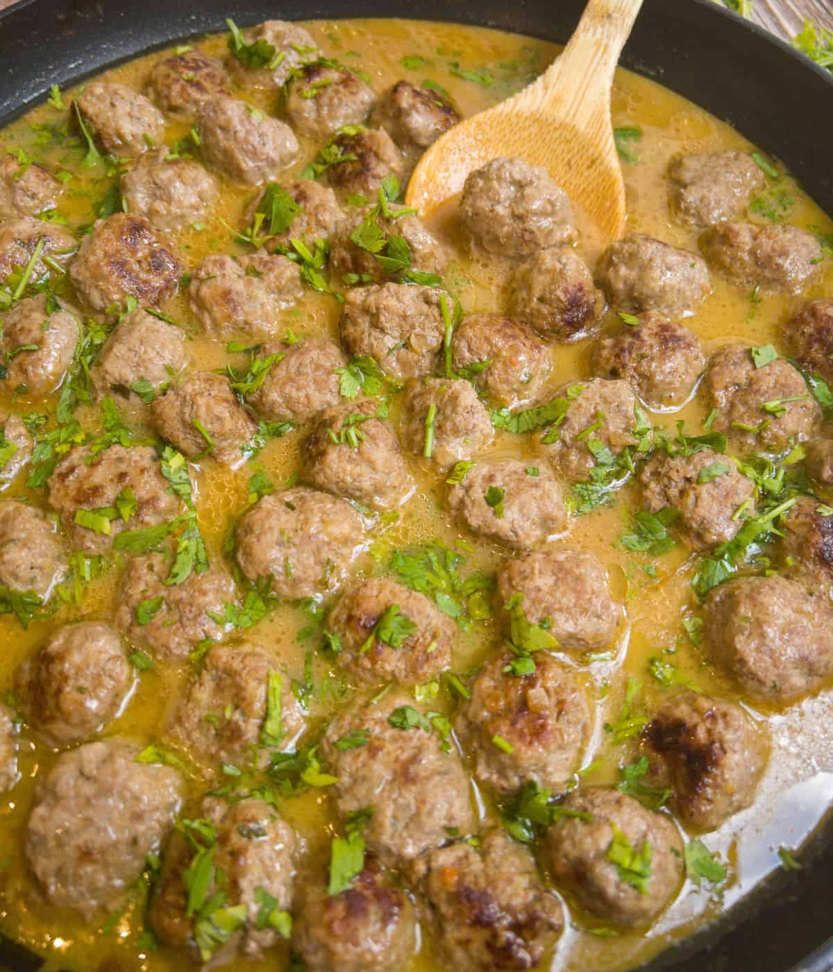close up of swedish meatballs in a frying pan with a wooden spoon