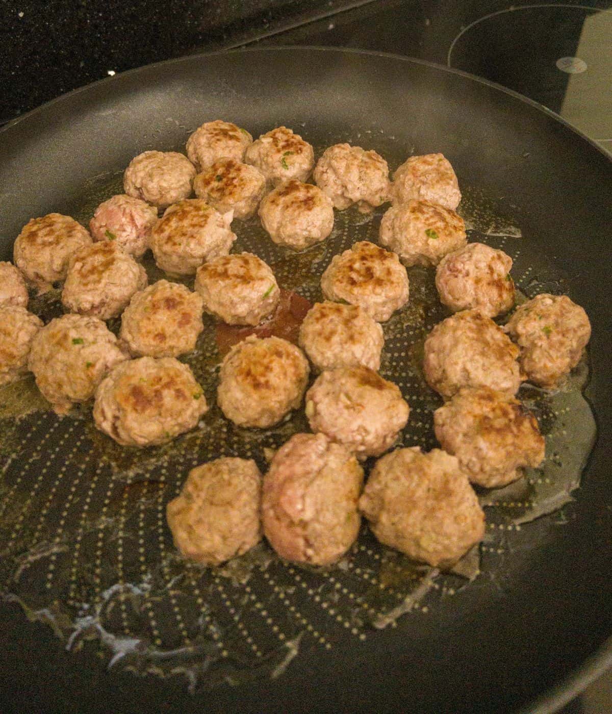 pork and beef meatballs cooking in a frying pan