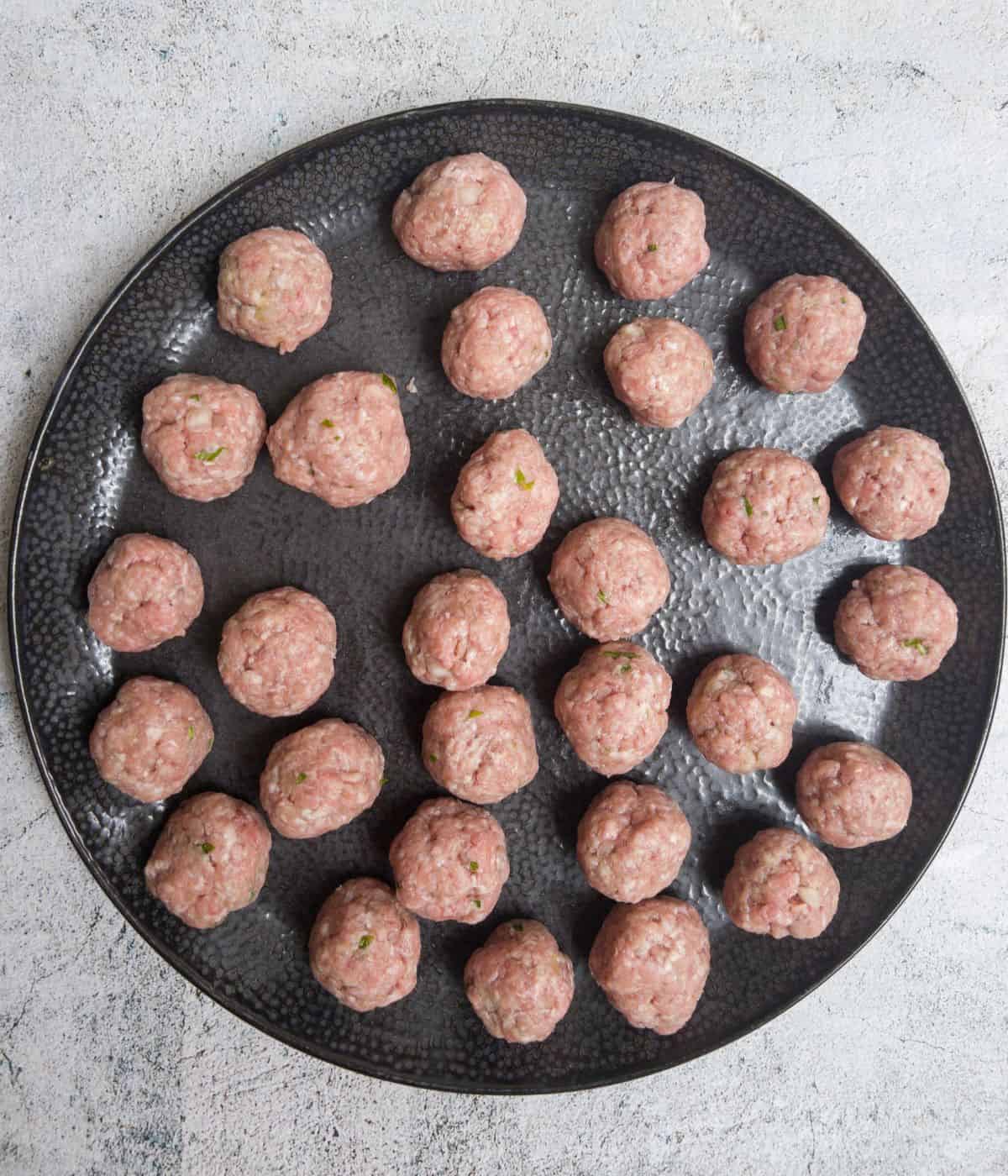 uncooked rolled meatballs on a black plate.