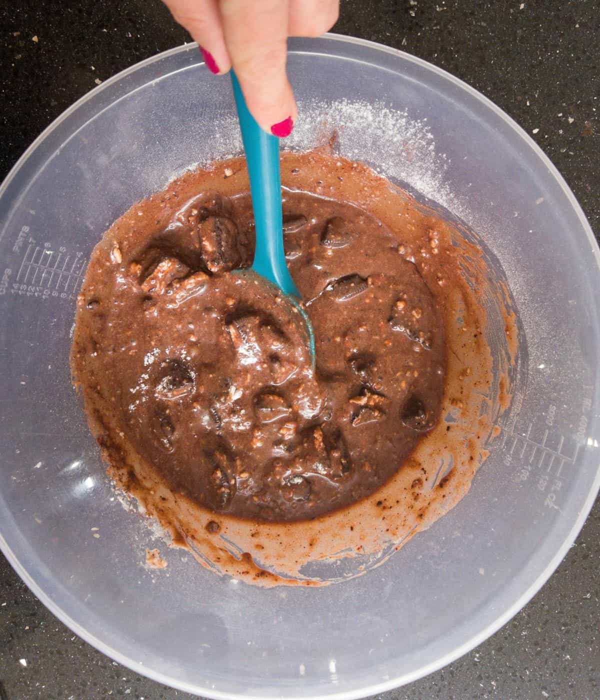 brownie mixture with broken oreo pieces mixed in being stirred in a mixing bowl.
