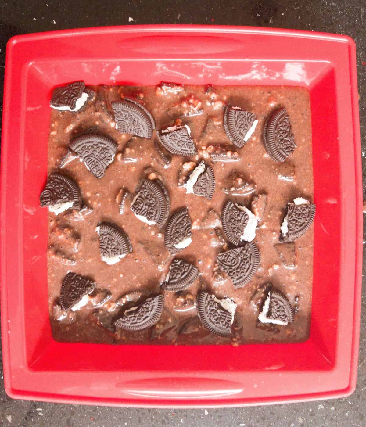 uncooked oreo brownie mixture in a red brownie baking tin.