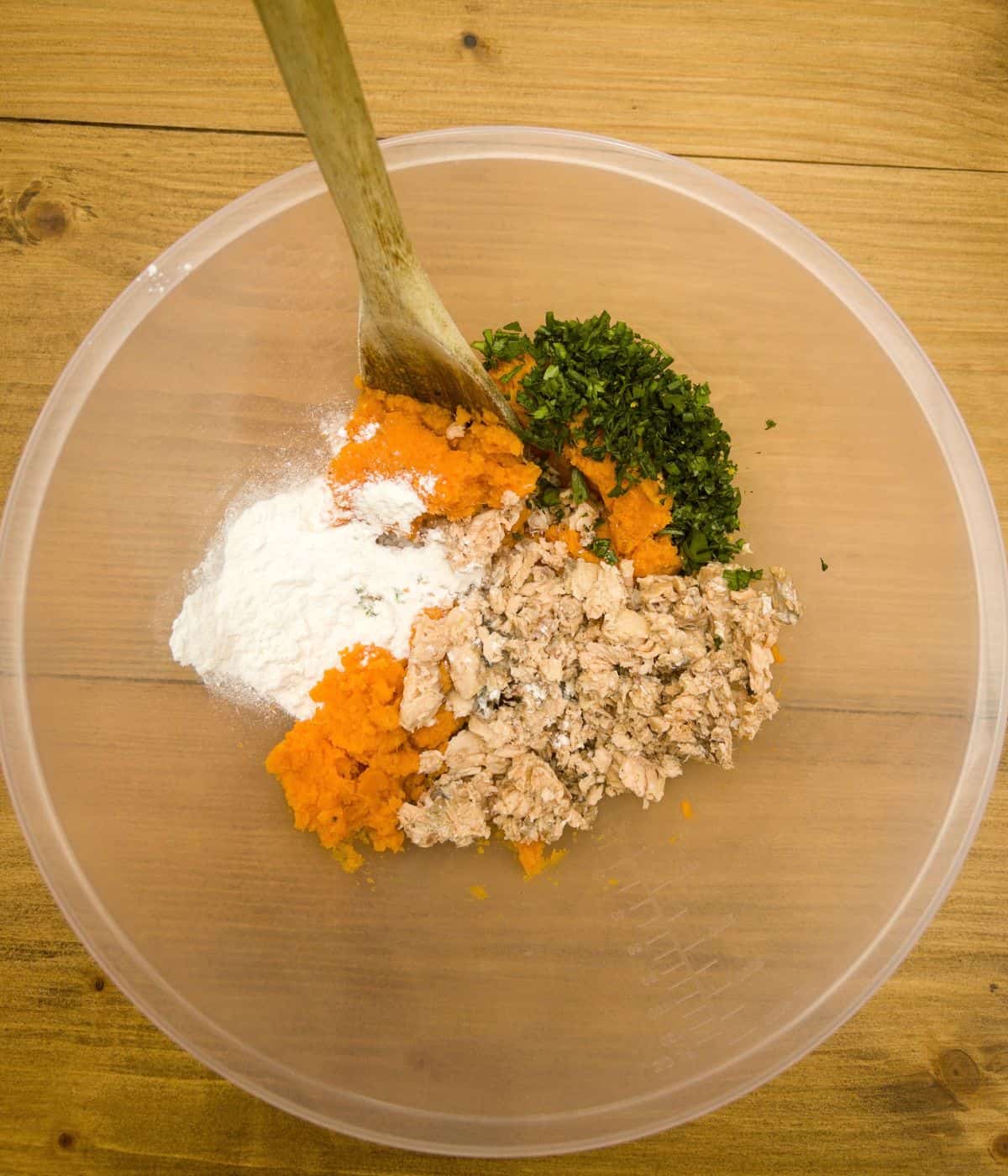 ingredients in a bowl to make salmon and sweet potato fishcakes with a wooden spoon in the bowl.