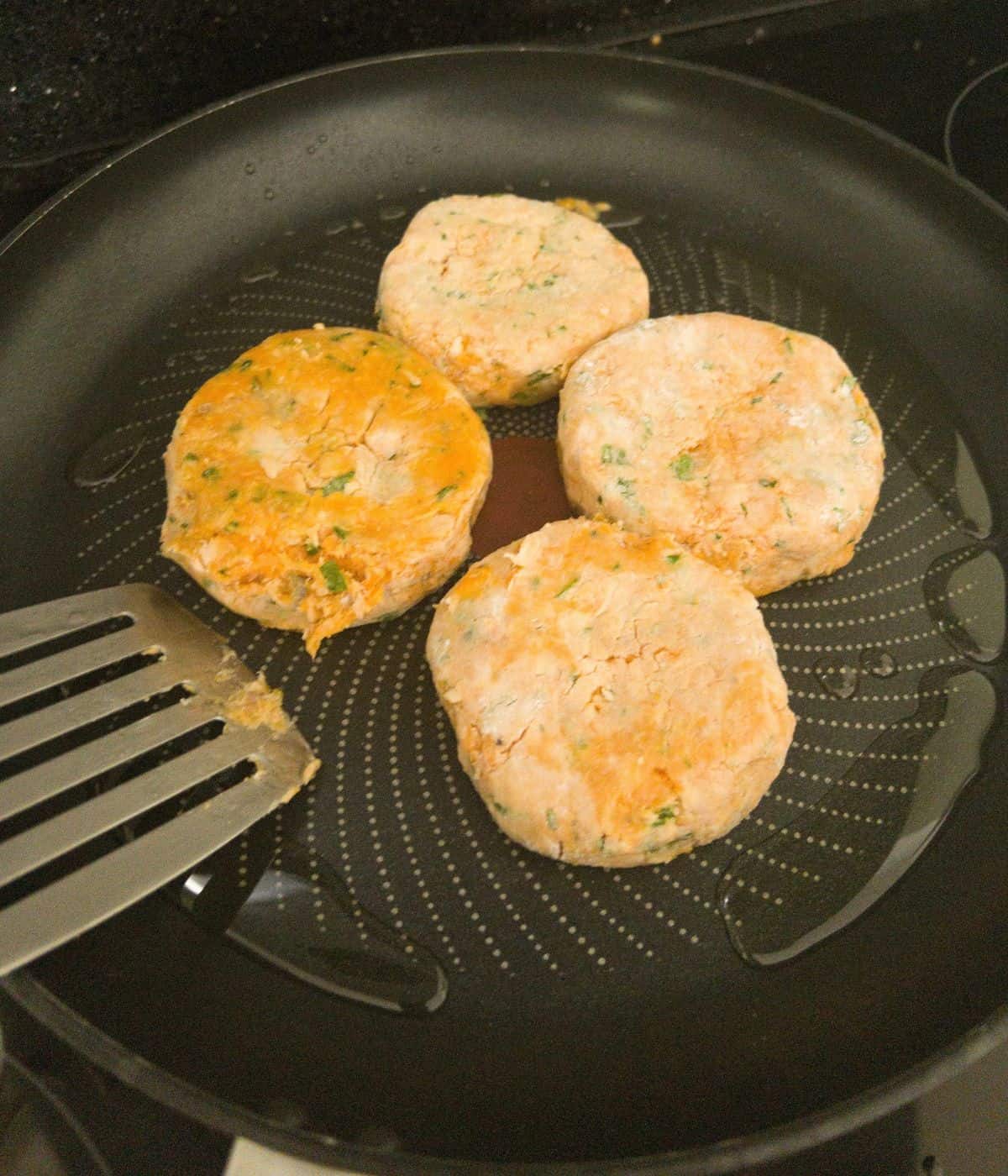 salmon fishcakes frying in a frying pan.