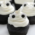 Chocolate cupcakes decorated with vanilla frosting and edible eyes to look like ghosts.