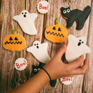 Selection of halloween cookies including ghosts, pumpkins and black cats, with a hand picking up the ghost cookie.