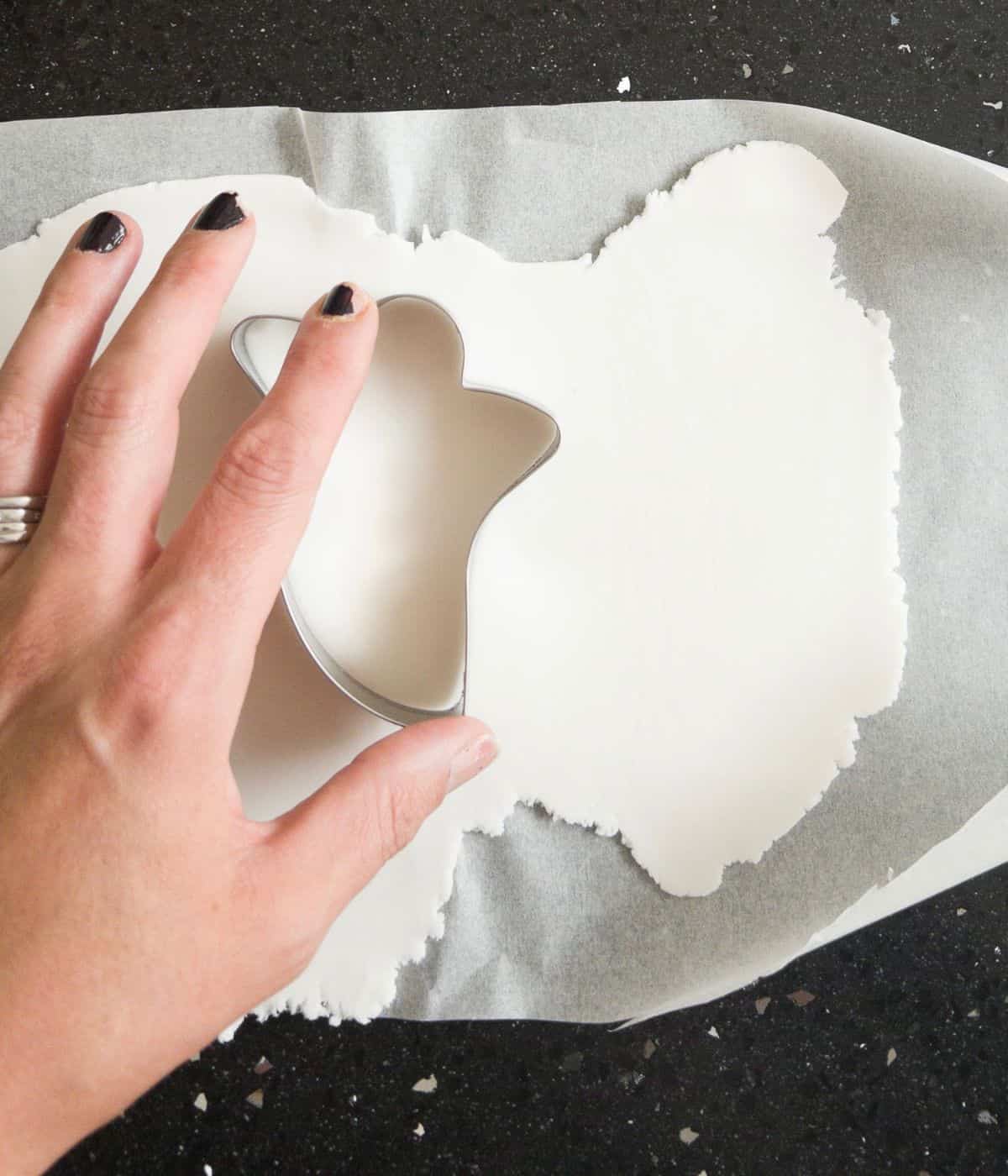ghost shape cookie cutter cutting out on white fondant icing,