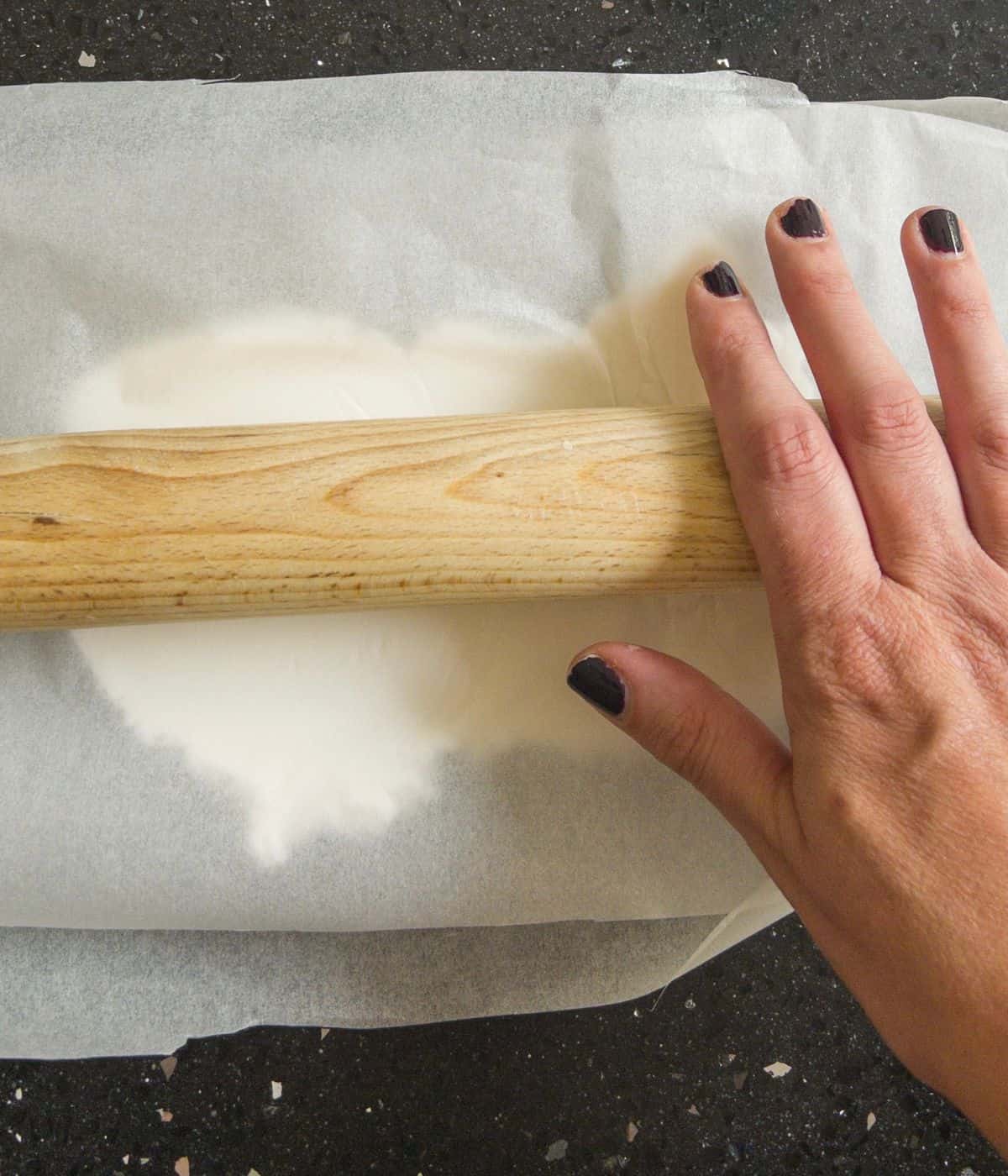 fondant icing being rolled out between two sheets of parchment paper.