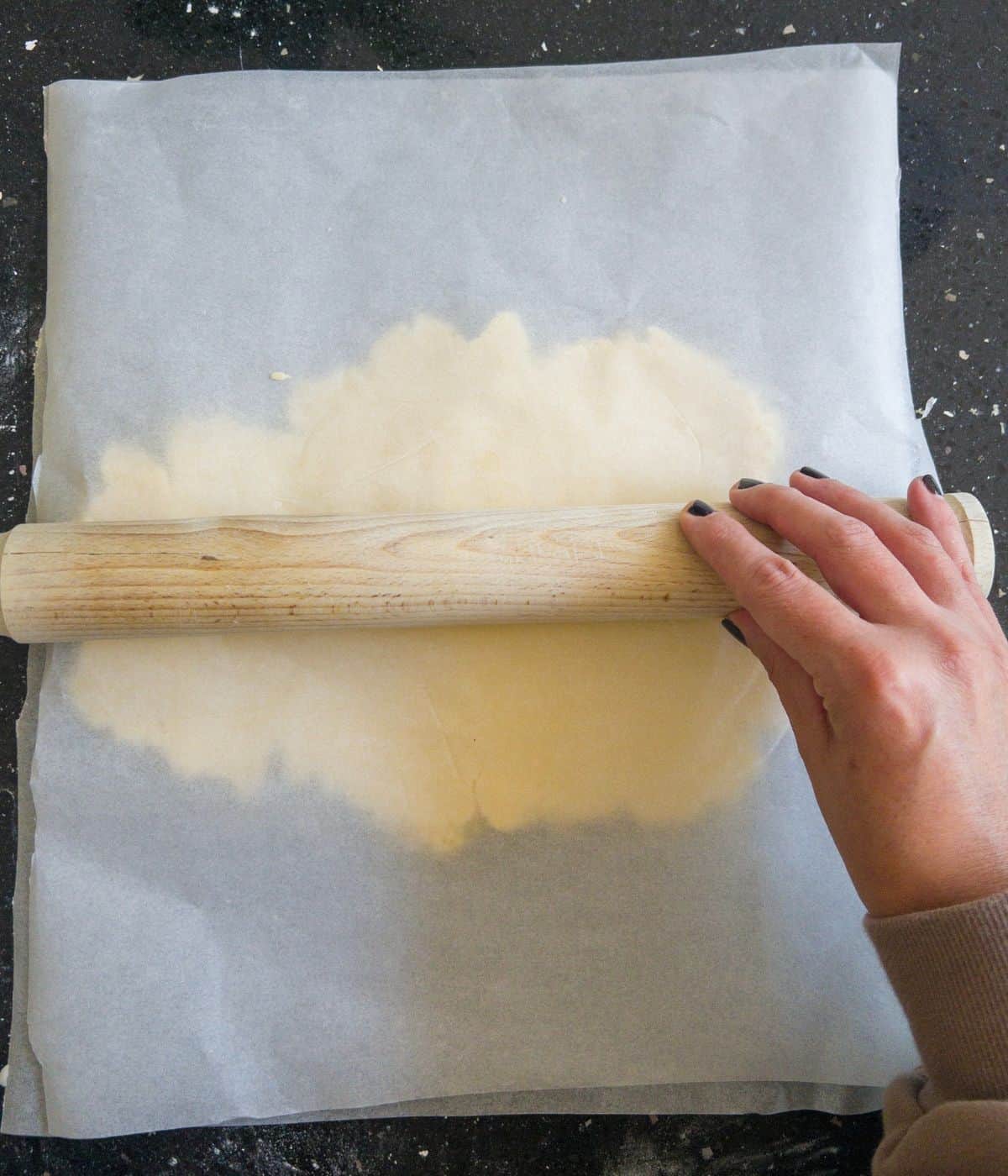 cookie dough being rolled out with a rolling pin between two sheets of greaseproof paper.