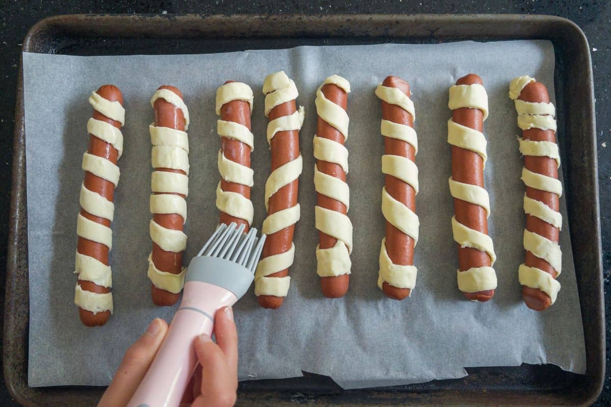 frankfurters wrapped in gluten free puff pastry being bastef with dairy free milk