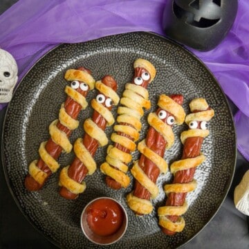 frankfurter mummies (puff pastry wrapped sausages) with edible eyes on a plate with a dip of ketchup