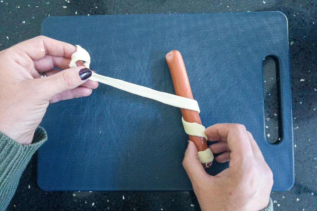 Puff pastry being rolled around a frankfurter.