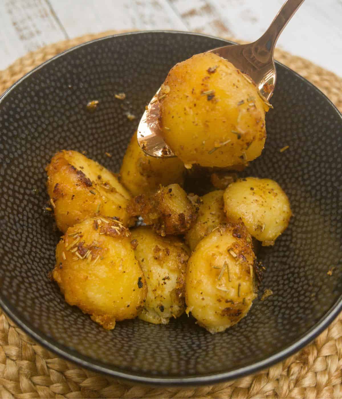 close up of slow cooker roast potatoes in a bowl with a spoon picking up one potato.