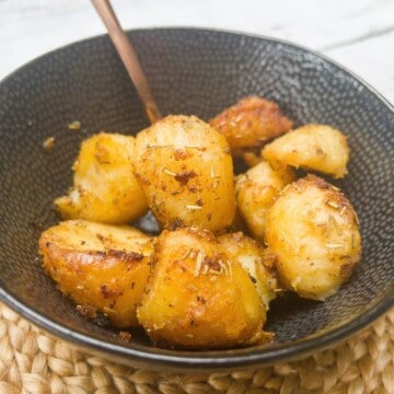 close up of roast potatoes in a bowl with a spoon.