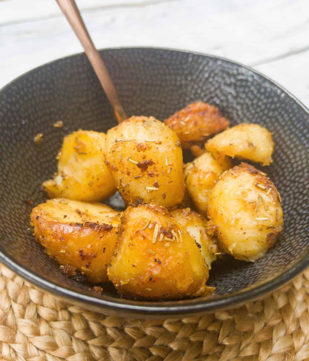 close up of roast potatoes in a bowl with a spoon.