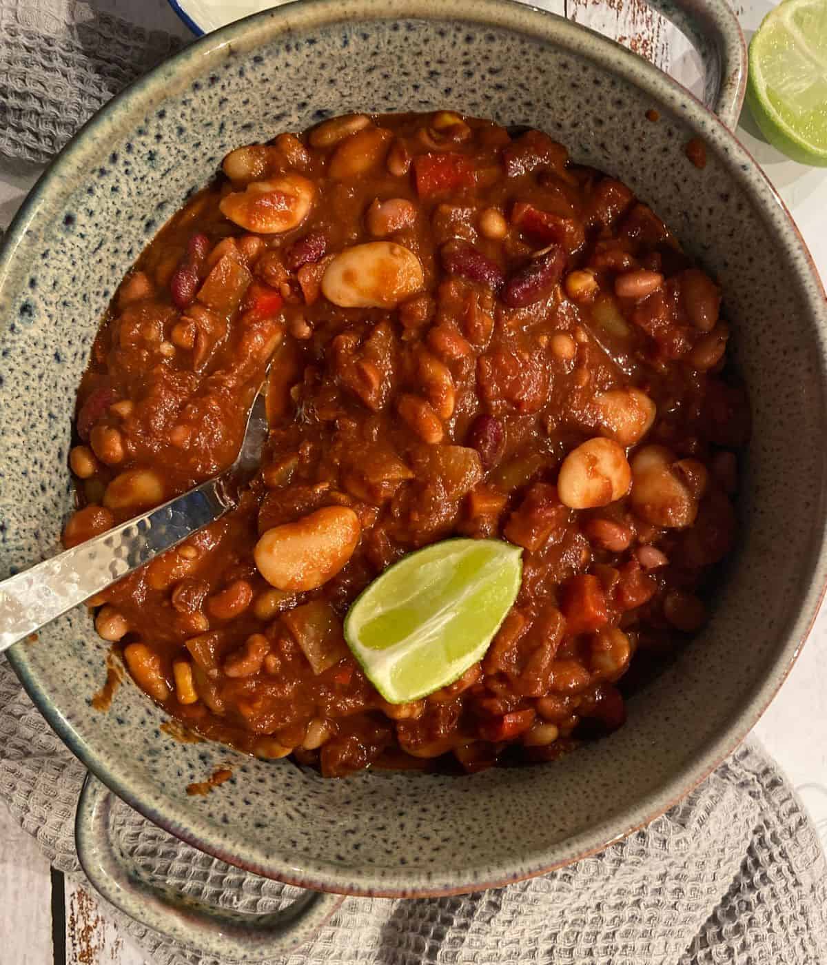 close up image of a pot of veggie bean chilli non carne garnished with lime.
