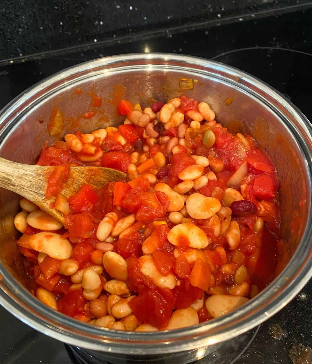 ingredients for mixed bean chilli cooking in a sauce pan including butter beans and kidney beans.