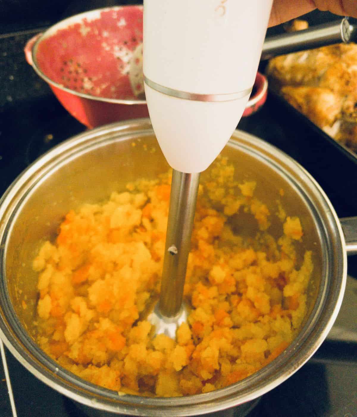 carrot and swede mashed being blended in a saucepan.