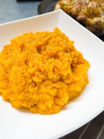 close up of carrot and swede mash in a white bowl with a roast chicken beside it.