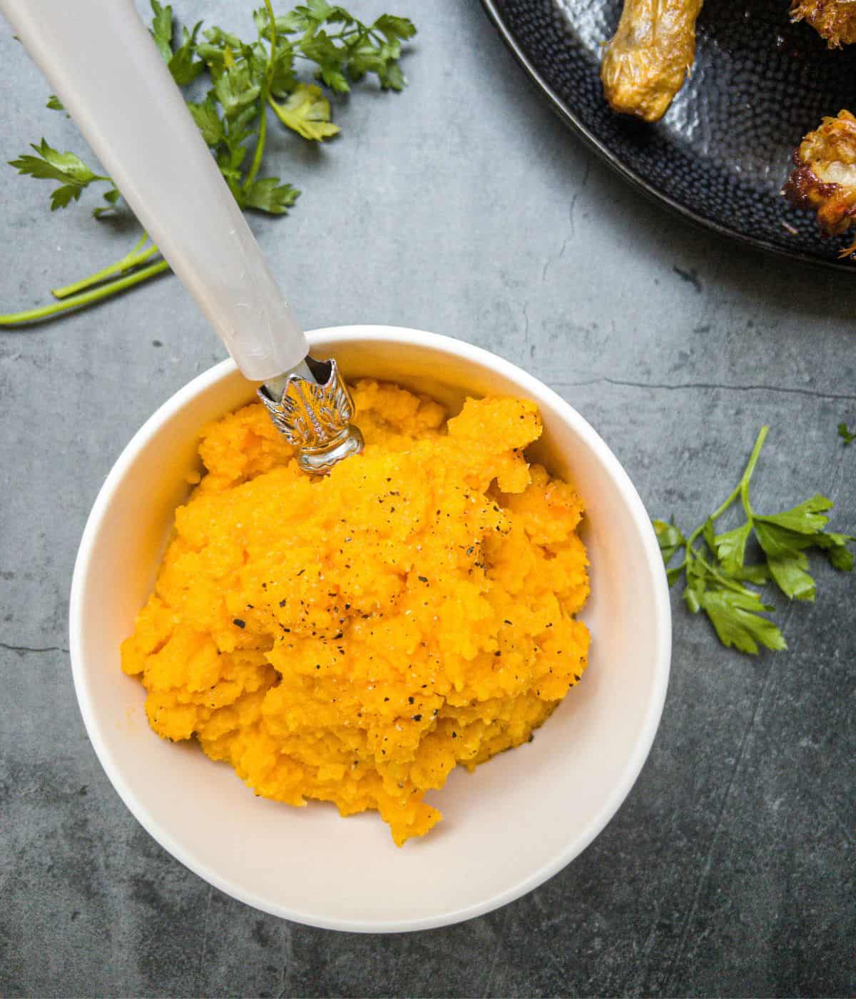 carrot and swede mash in a bowl with a spoon.