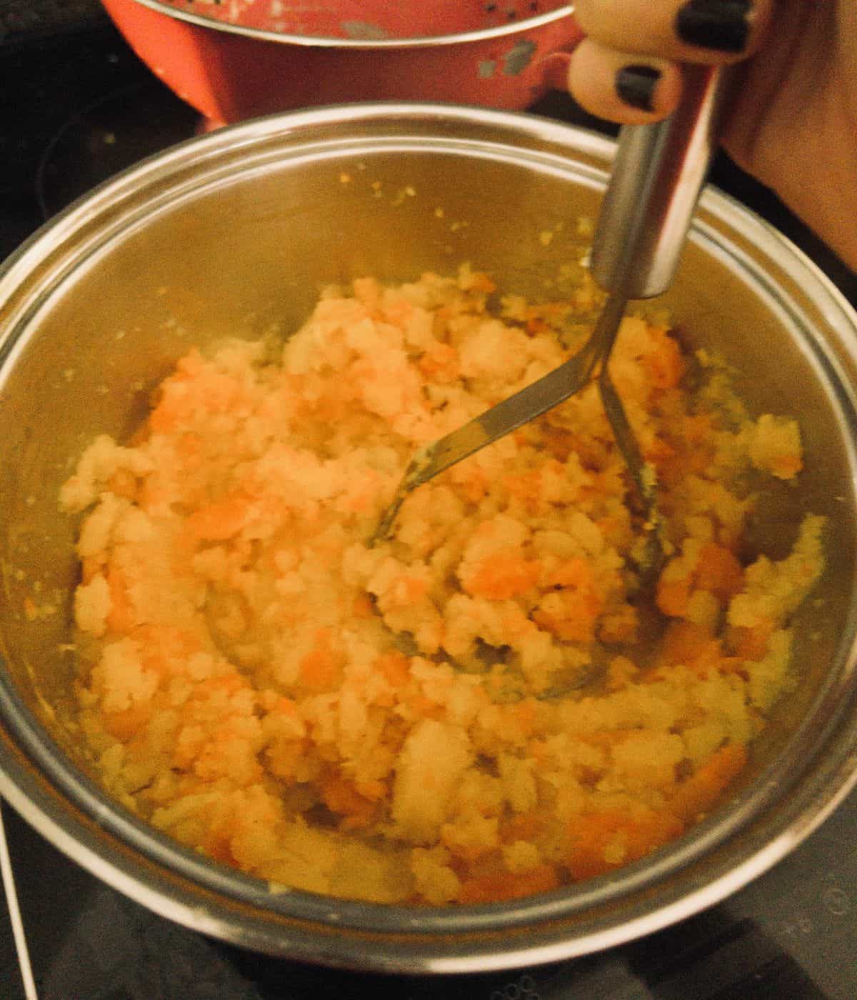 carrot and swede being mashed in a saucepan.
