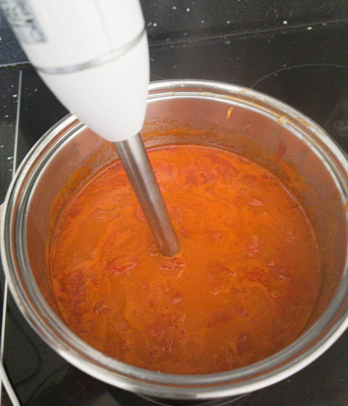 tomato soup being blended in a saucepan with a hand blender.