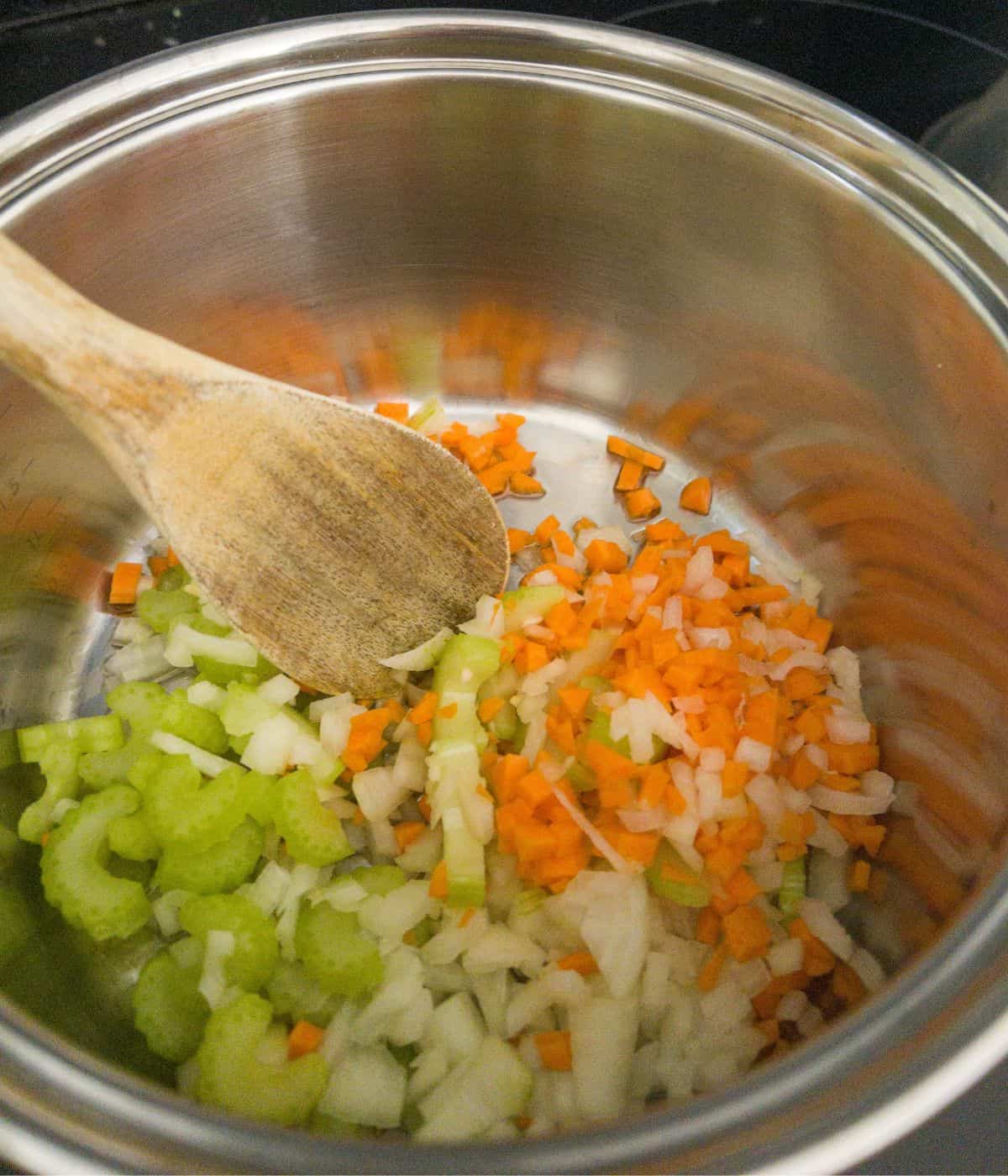 garlic, celery, onion and carrot cooking in a saucepan being stirred with a wooden spoon.