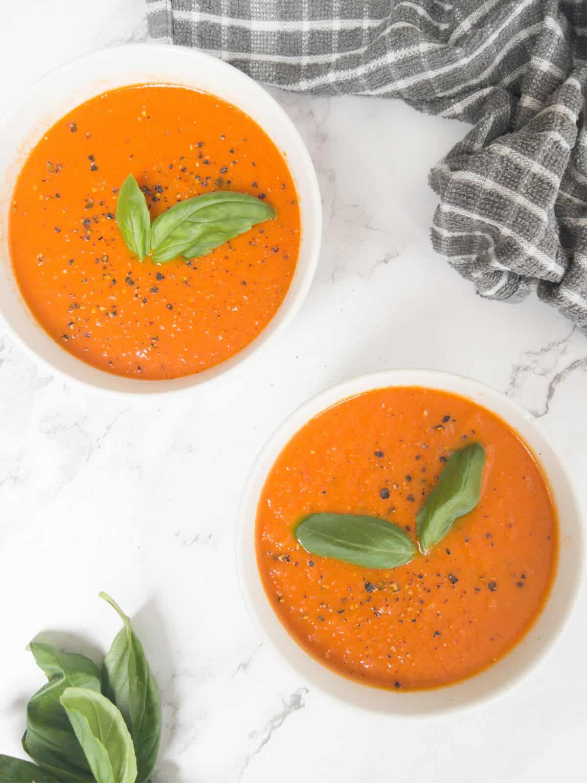 two bowls of gluten free tomato soup in white bowls garnished with basil