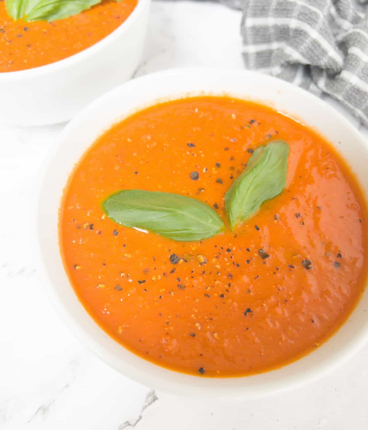 bowl of gluten free tomato soup garnished with basil in a white bowl.