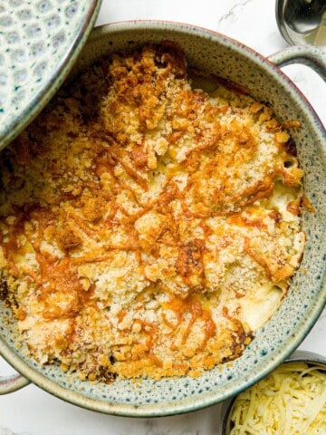 Cauliflower cheese in a casserole dish with the lid propped on the side, with a side bowl of cheese.