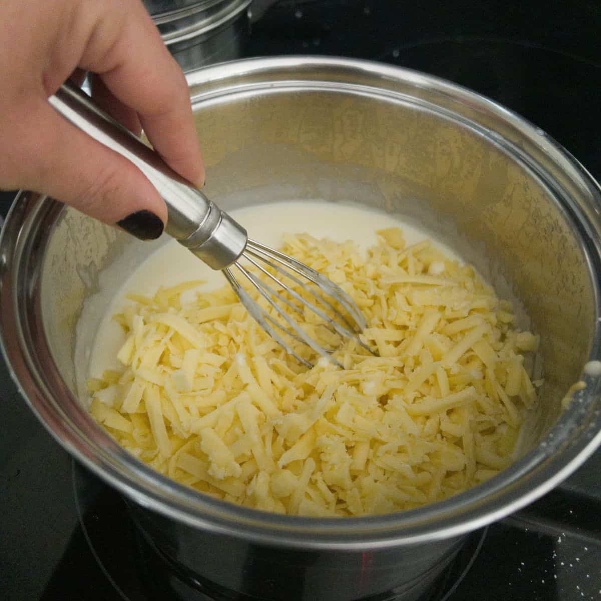 cheese sauce being made in a saucepan with cheese being whisked in.