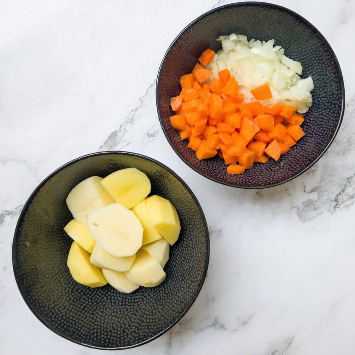 two black bowls, one containing chopped potatoes and the other chopped carrot and onion.
